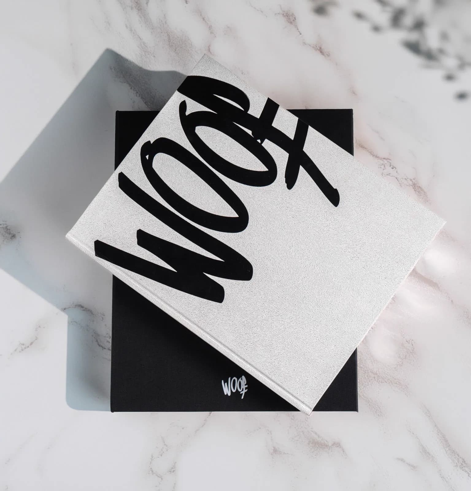 La portada blanca de WOOF sobre su caja, fotografiada sobre mármol
